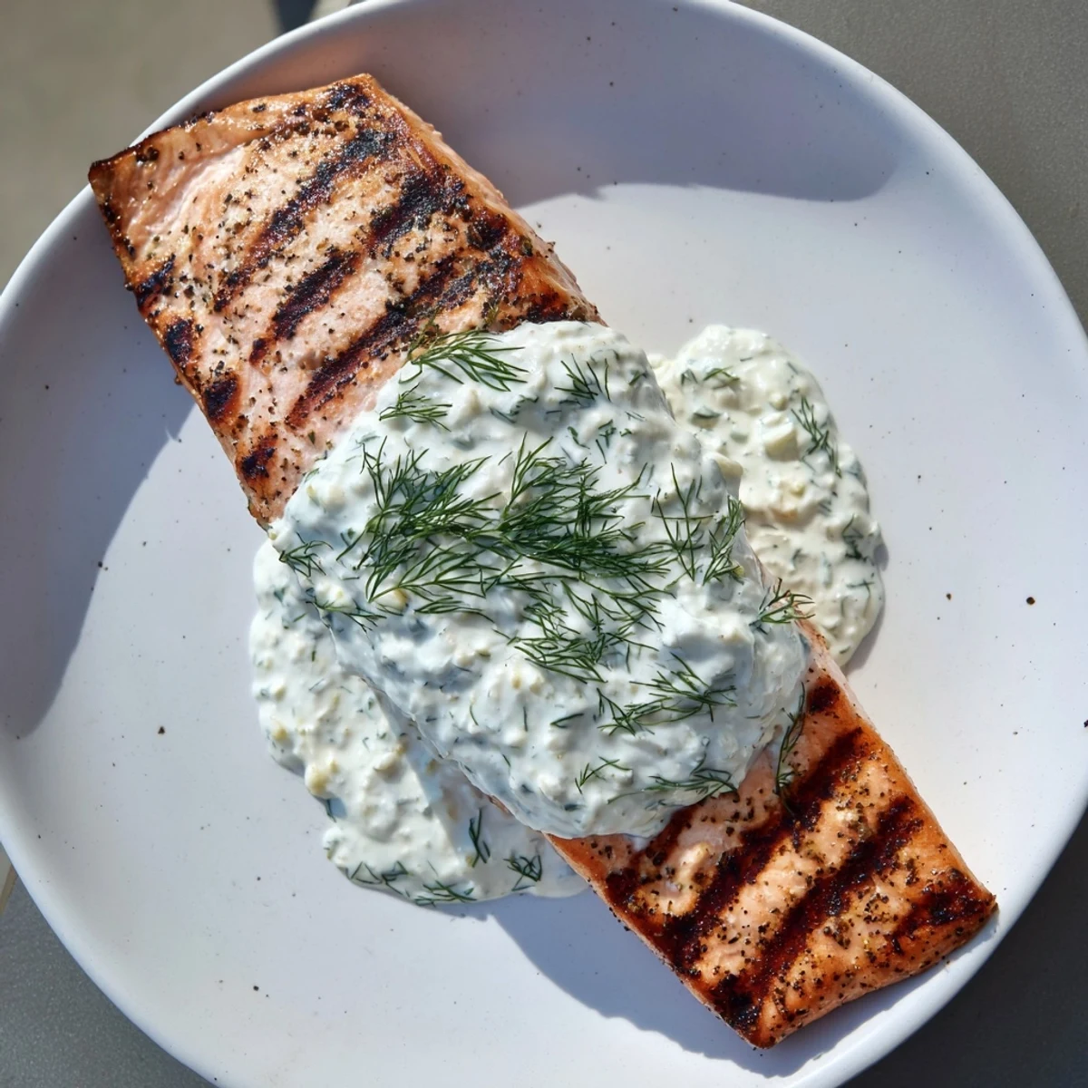A close-up of flaky grilled salmon topped with fresh dill yogurt sauce, ready for dinner tonight.