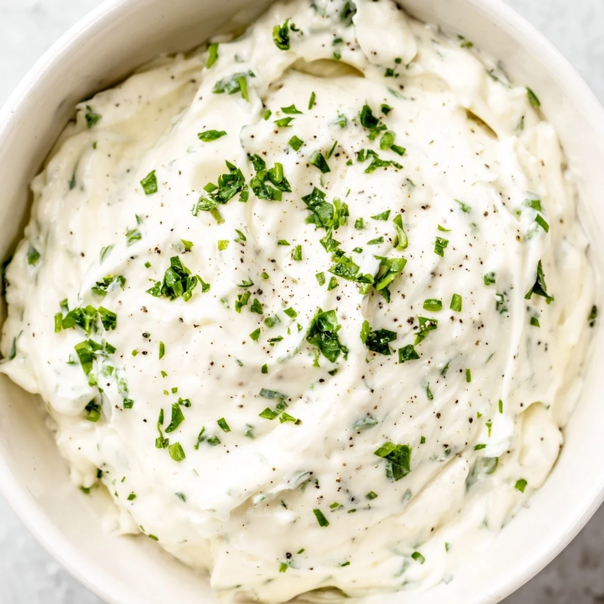 A creamy garlic dip, a swirl of white with flecks of green herbs, ready for dipping.