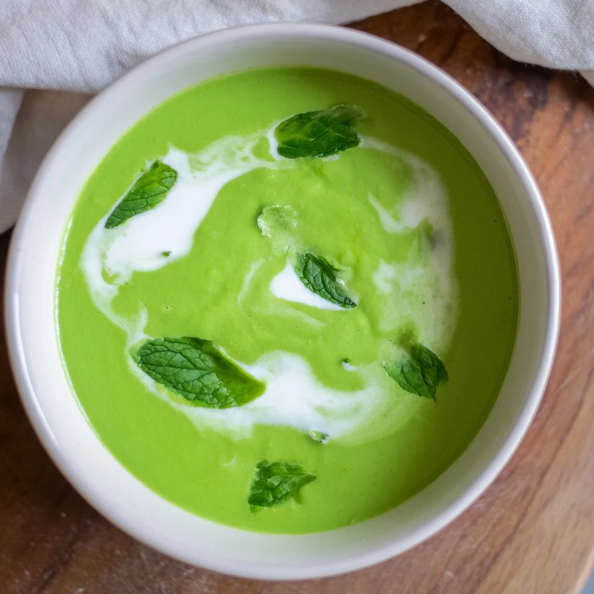 Smooth, vibrant green creamy pea soup in a bowl, swirled with extra cream, ready to enjoy.