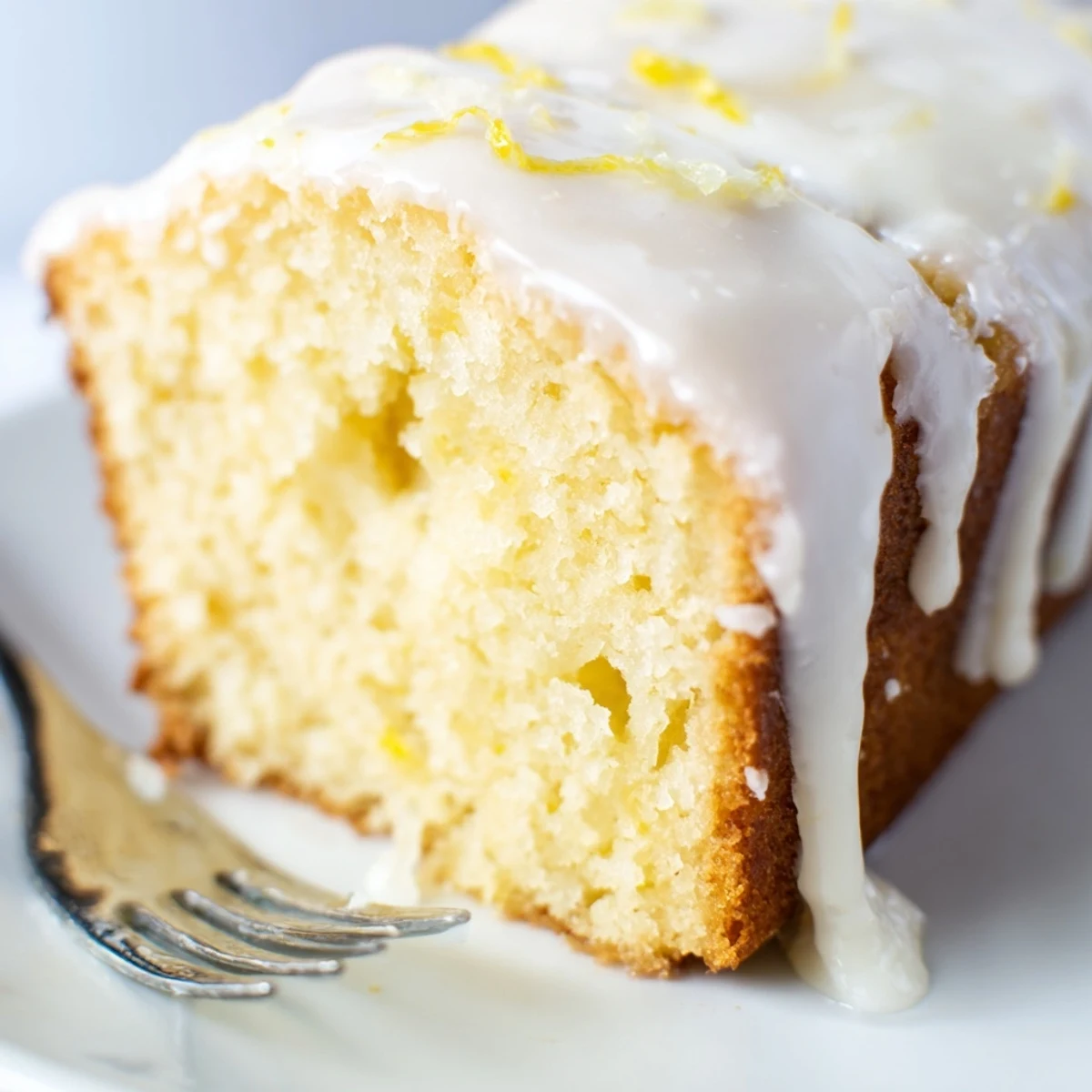 A slice of Lemon Loaf showing a moist, tender crumb next to a steaming mug of tea.