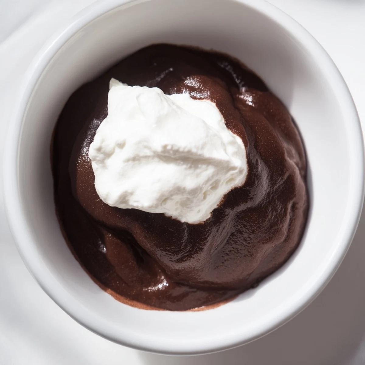 A chilled glass dish of silky chocolate pudding crowned with fluffy whipped cream, ready for dessert.