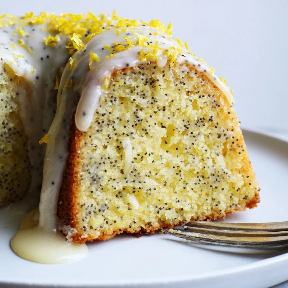 Freshly glazed Lemon Poppy Seed Bundt Cake slices on a plate, garnished with lemon zest and a dollop of whipped cream.