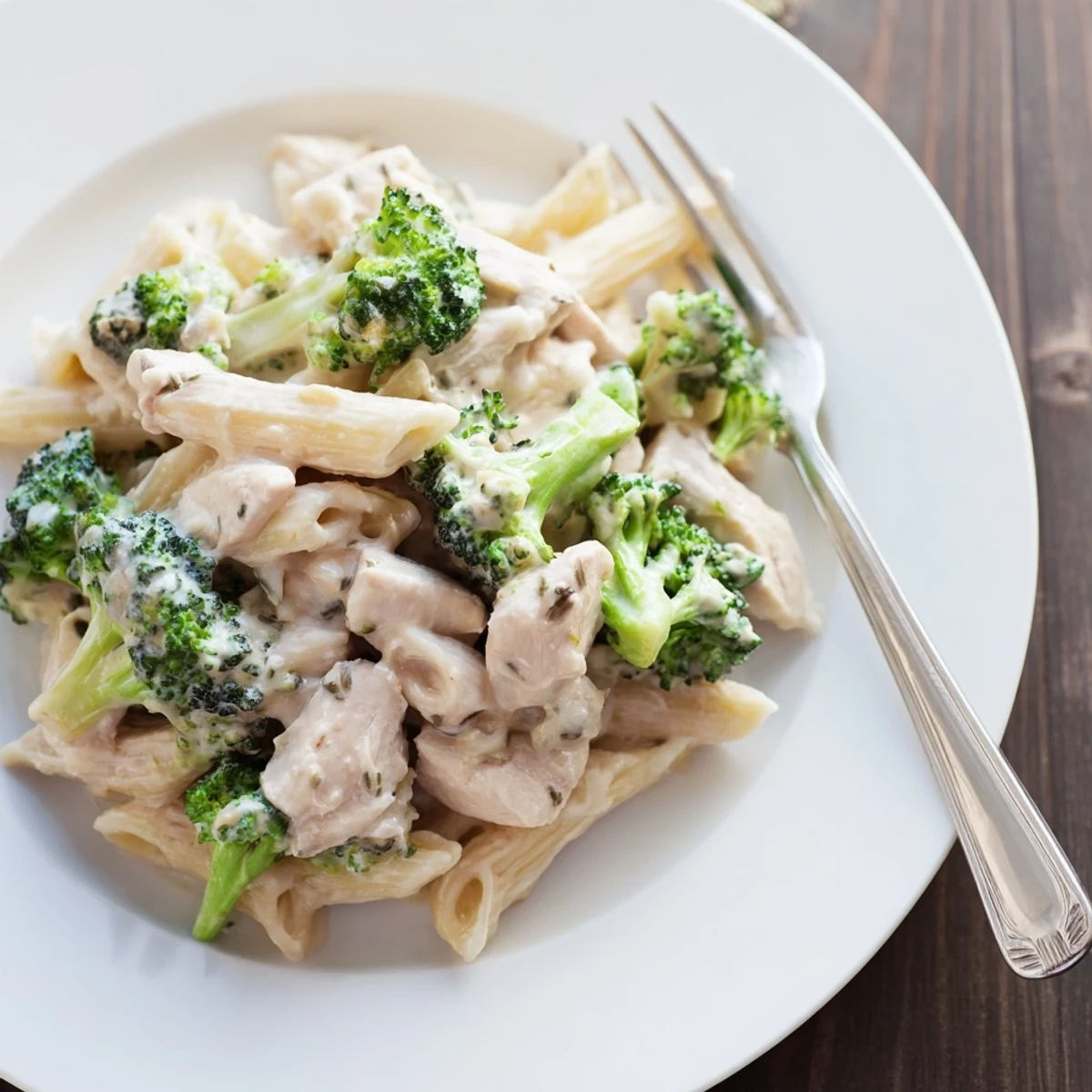 A close-up view of Creamy Broccoli Pasta with Chicken on a white plate, garnished with fresh parsley and extra grated Parmesan, ready for a comforting dinner.