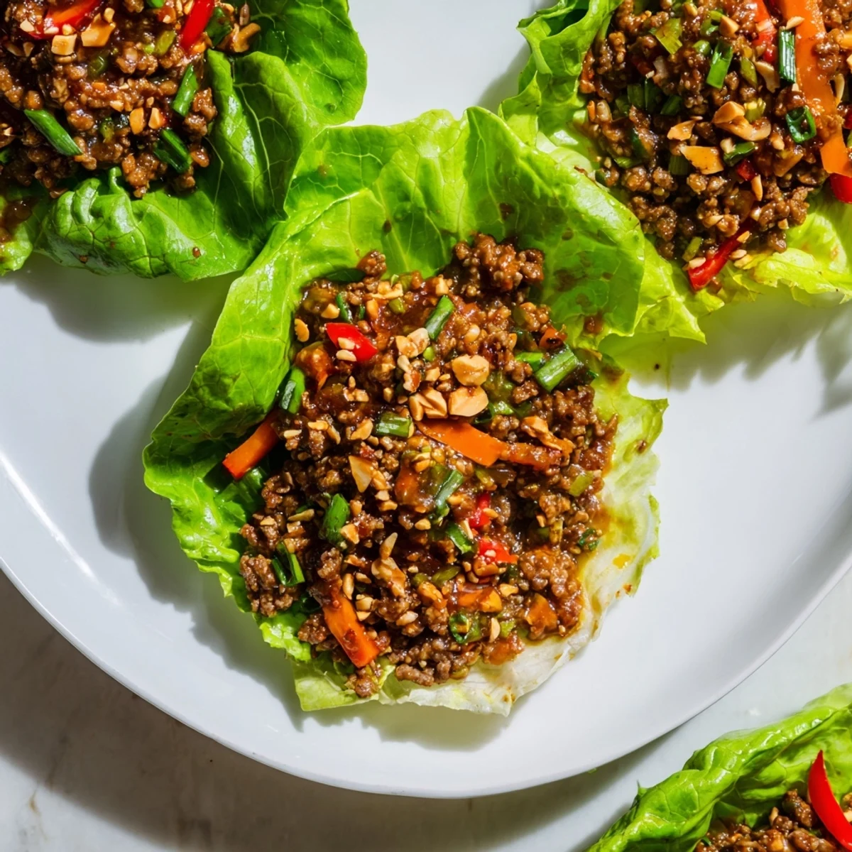 Tender lettuce leaves holding a hearty filling of beef, vegetables, and sesame, garnished with chopped peanuts and fresh cilantro.