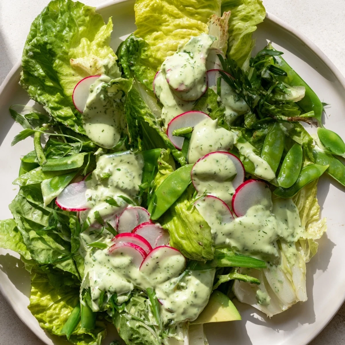 A close-up of Green Salad with Green Goddess Dressing, featuring creamy avocado slices and crisp cucumber on vibrant greens.