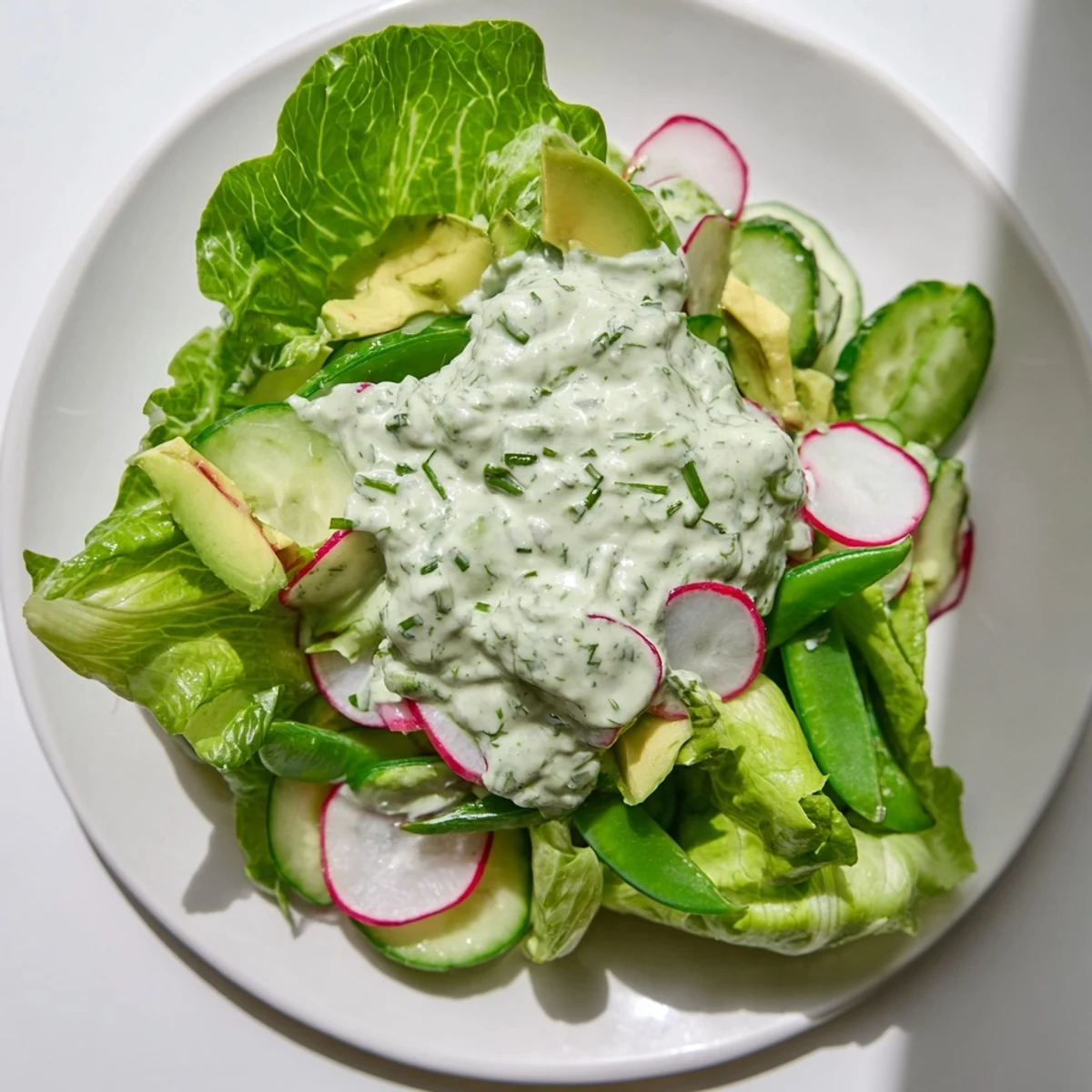 Served in a white bowl, the Green Salad with Green Goddess Dressing is tossed with radishes and fresh herbs.