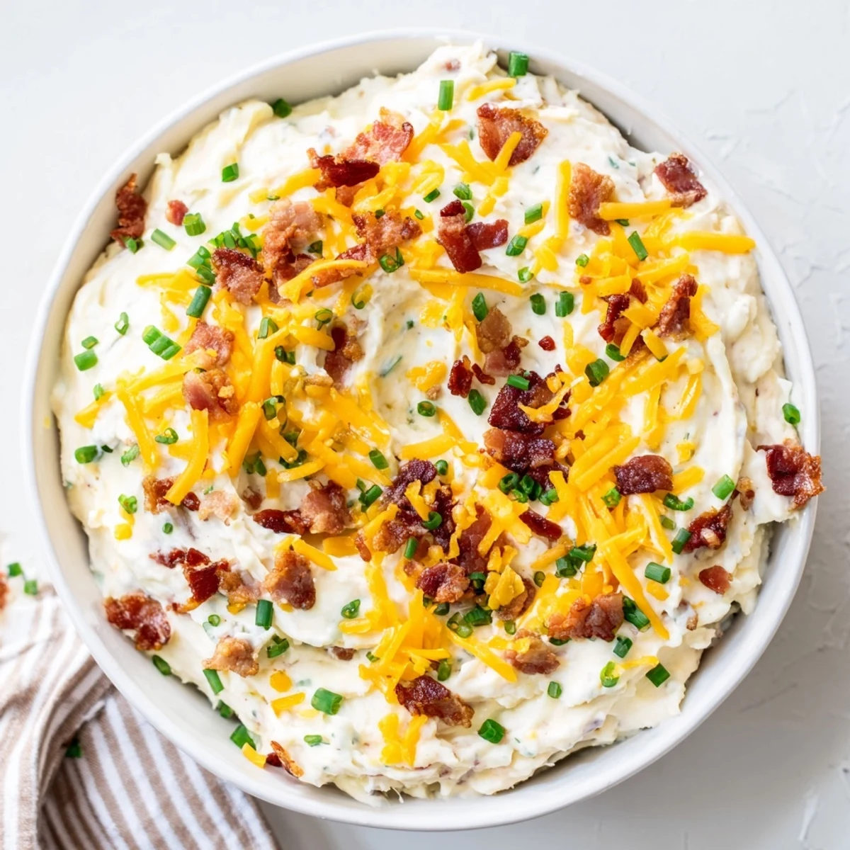Stirring together sour cream and cheddar for a cold Super Bowl Loaded Baked Potato Dip garnished with fresh chives.