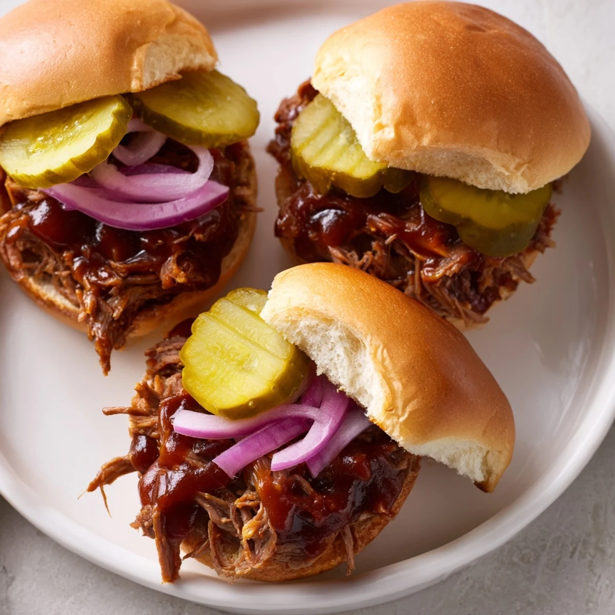 Golden, slow-cooked pulled beef mounded on toasted slider buns, garnished with crisp red onion and dill pickles.