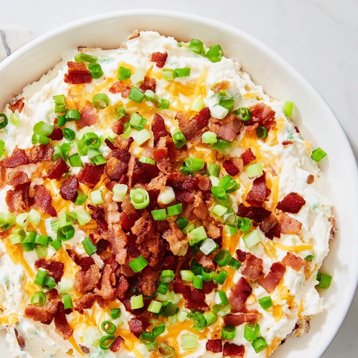 A bowl of Loaded Baked Potato Dip topped with crumbled bacon and green onions, paired with thick-cut potato chips on a rustic serving platter.  