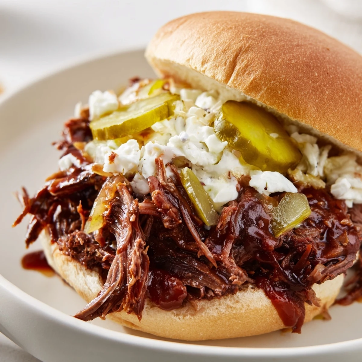 A close-up of Slow Cooker Pulled Beef Sandwiches with tender shredded meat piled high on a toasted bun, topped with creamy coleslaw and crisp pickle slices.