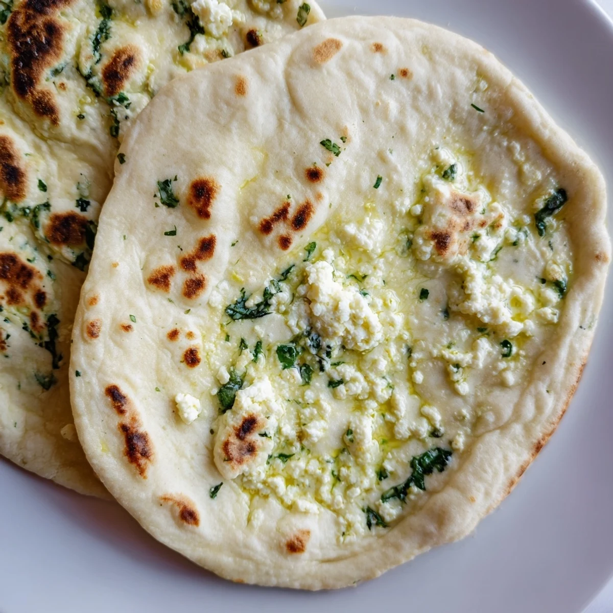 Warm Cottage Cheese Garlic Naan stacked on a plate, garnished with chopped cilantro and garlic.