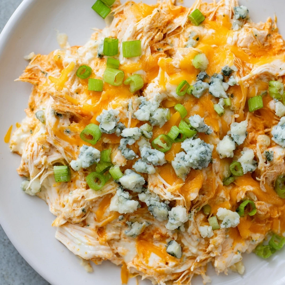 A close-up view of creamy Keto Buffalo Chicken Dip with shredded chicken and spicy buffalo sauce, garnished with green onions and blue cheese crumbles.