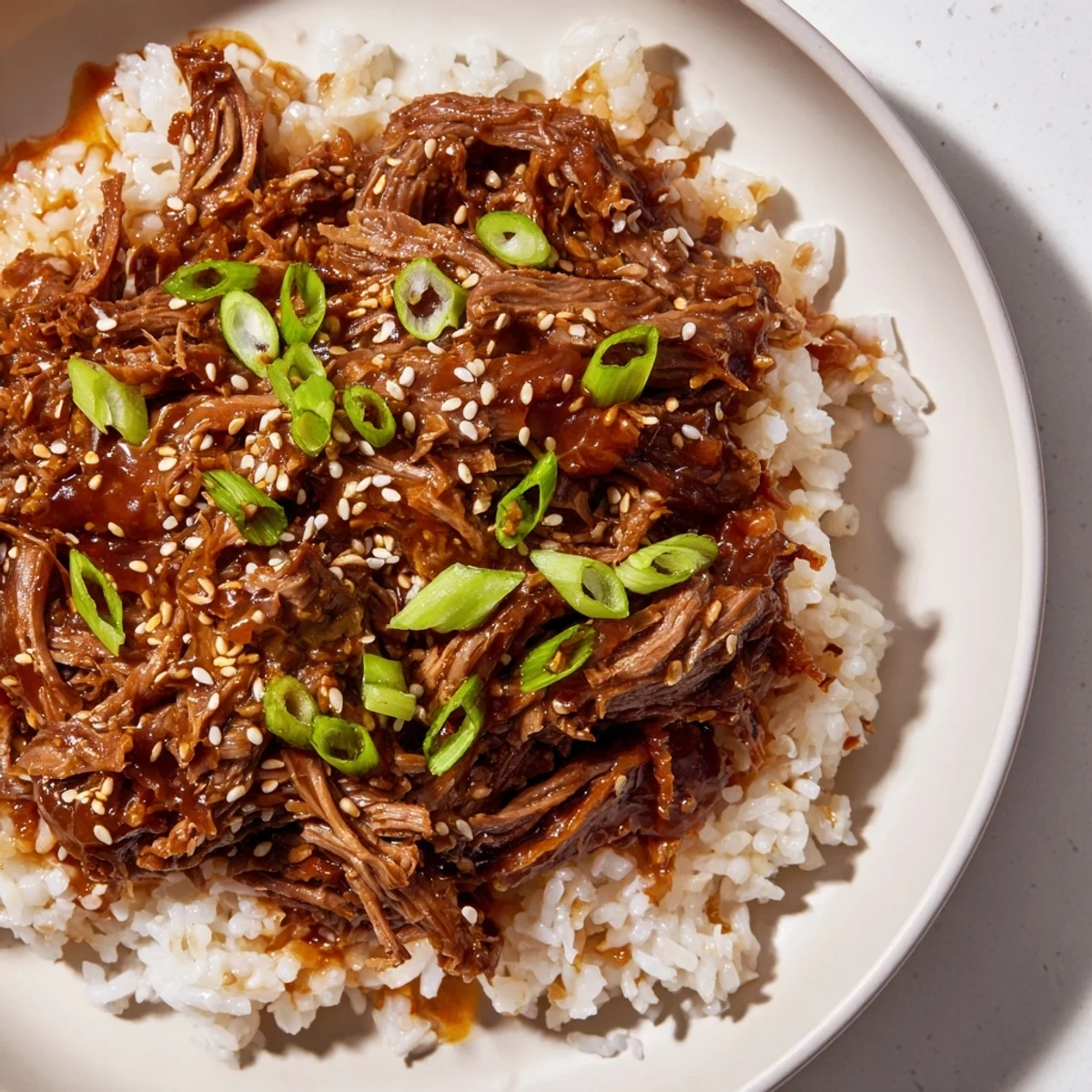 Slow-cooked Crock Pot Korean Beef tenderly shredded and swimming in a glossy, savory-sweet sauce, served over fluffy white rice.