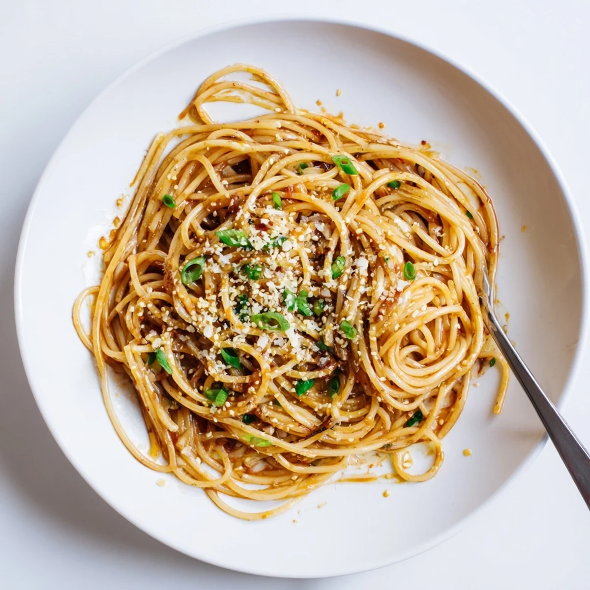 Close-up of Garlic Noodles glistening with rich soy-butter sauce, garnished with chopped scallions on a white plate.