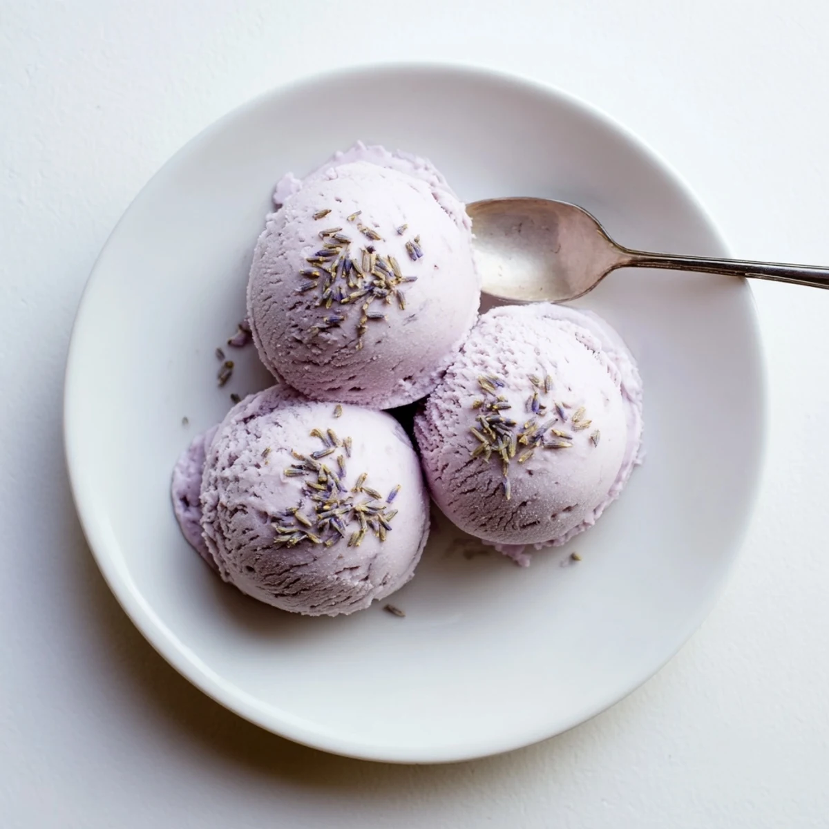 Creamy Lavender Ice Cream in a white bowl with a vintage spoon, topped with dried lavender buds.