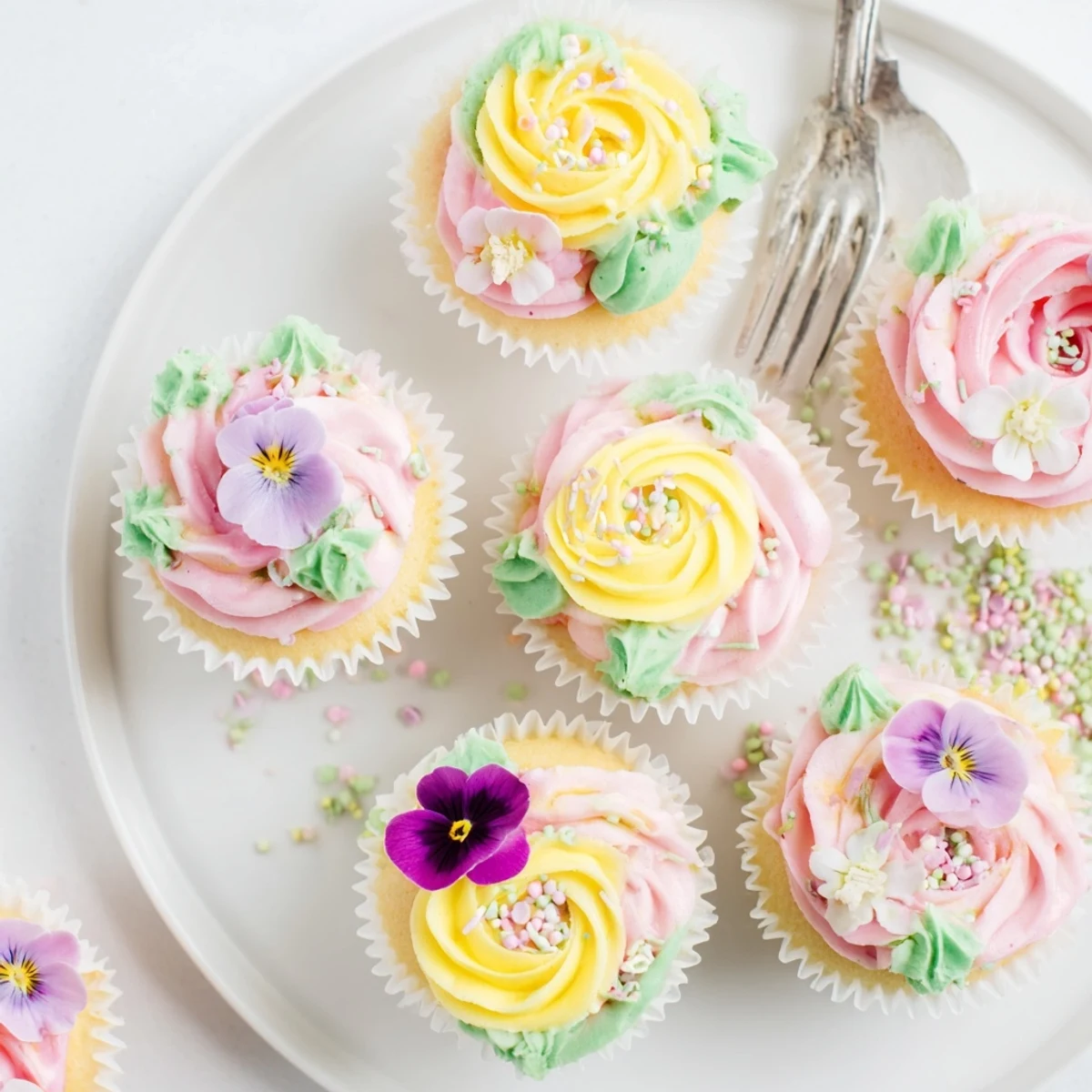 A close-up of Baby In Bloom Cupcakes decorated with pink and yellow buttercream flowers and edible pansies.