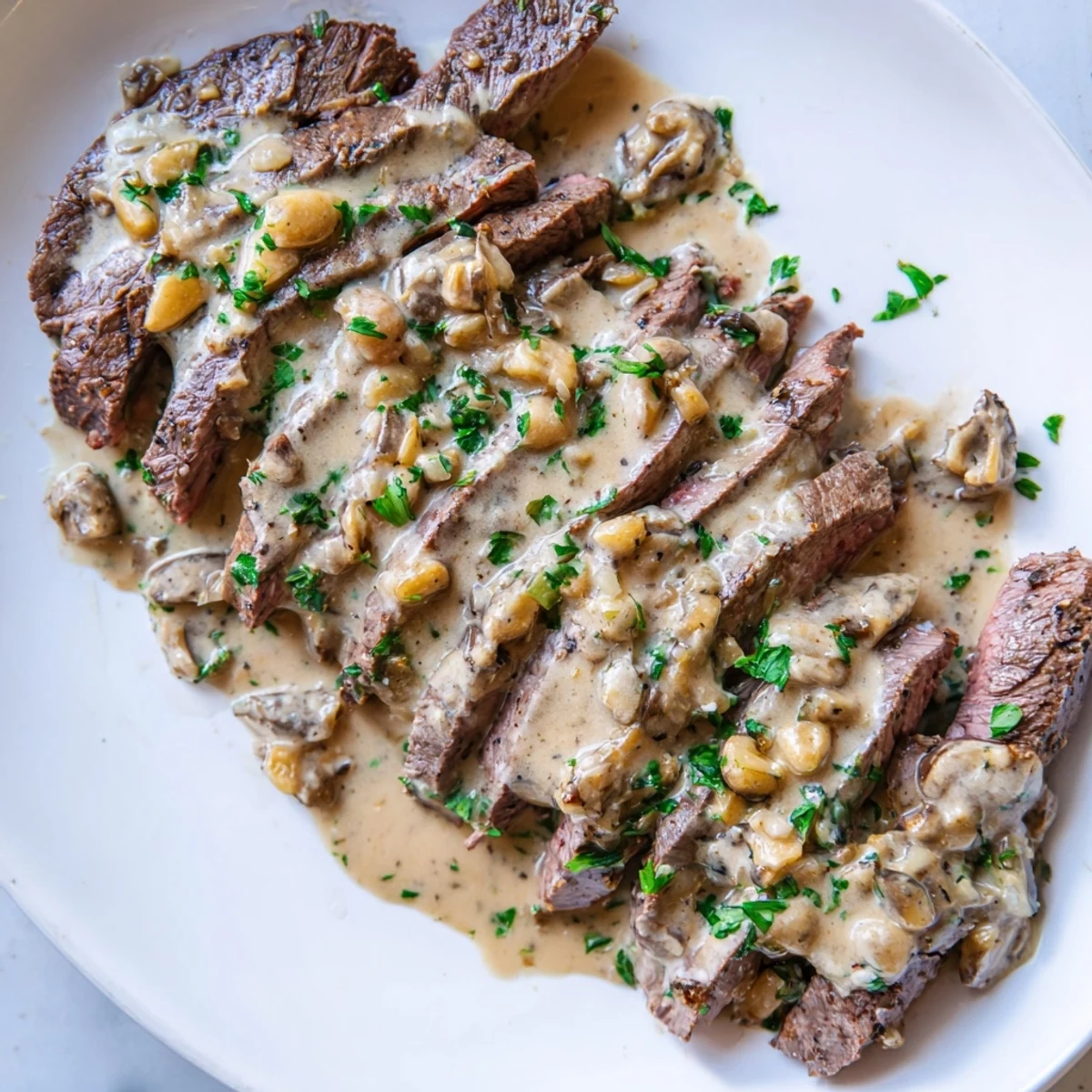Juicy flank steak slices fanned out with drizzled roasted garlic sauce and fresh parsley garnish for a special meal.