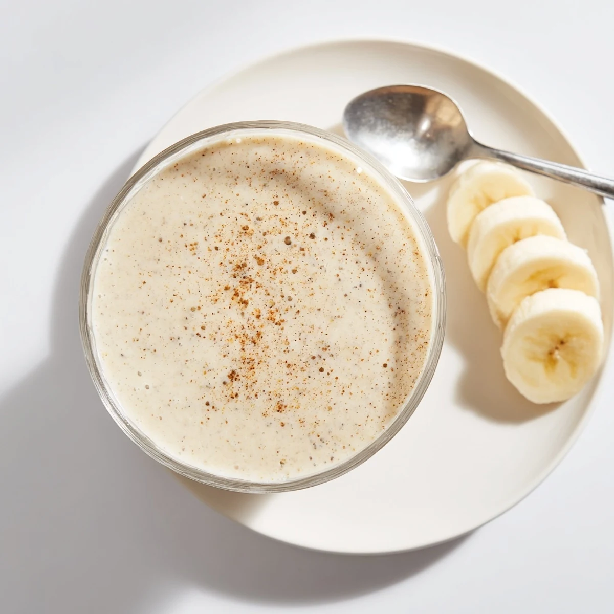 Tall glass of creamy Greek yogurt banana smoothie garnished with fresh banana slices