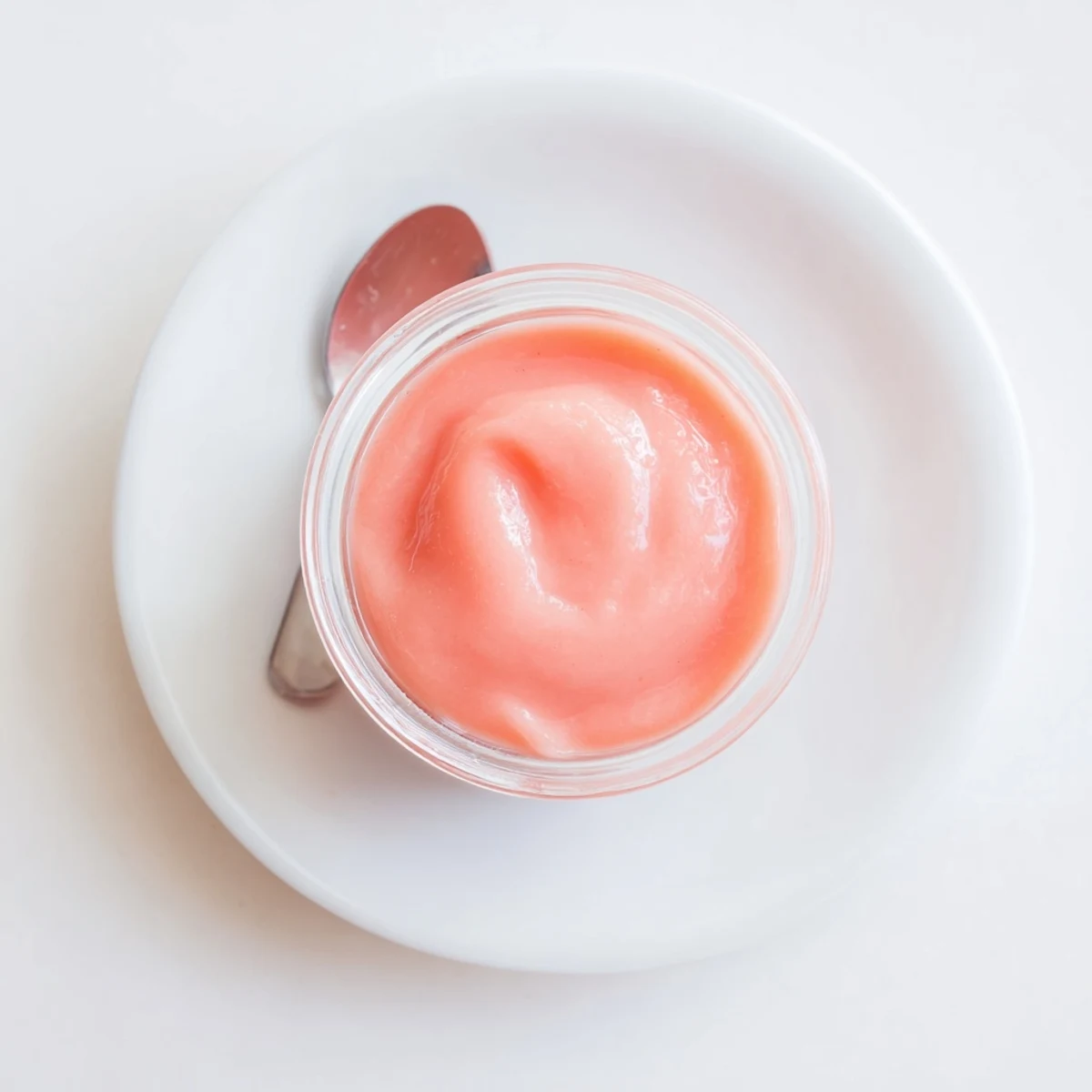 Creamy pink lemon curd in a glass jar with a small spoon resting on top