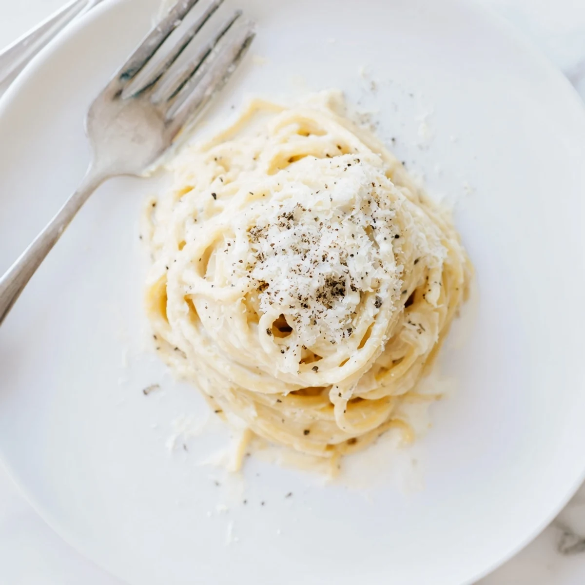 Creamy Cacio e Pepe pasta with glossy cheese coating and freshly ground black pepper on a white plate