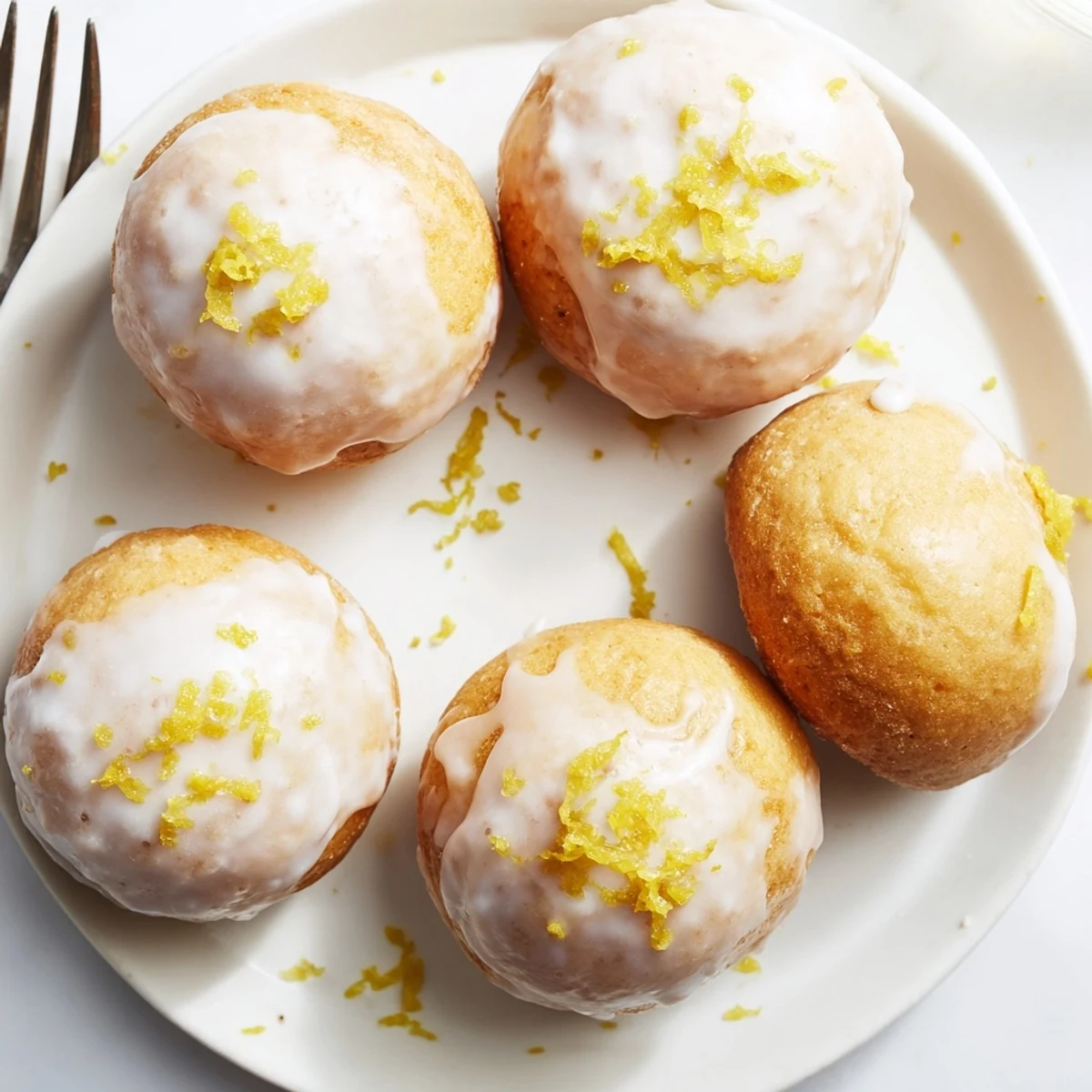 Bright lemon glazed mochi donuts arranged on white plate with powdered sugar dusting