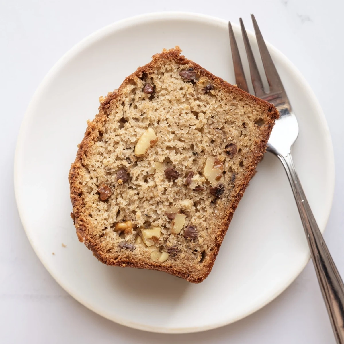 Golden brown moist banana bread loaf with a cracked top, sliced on a wooden board