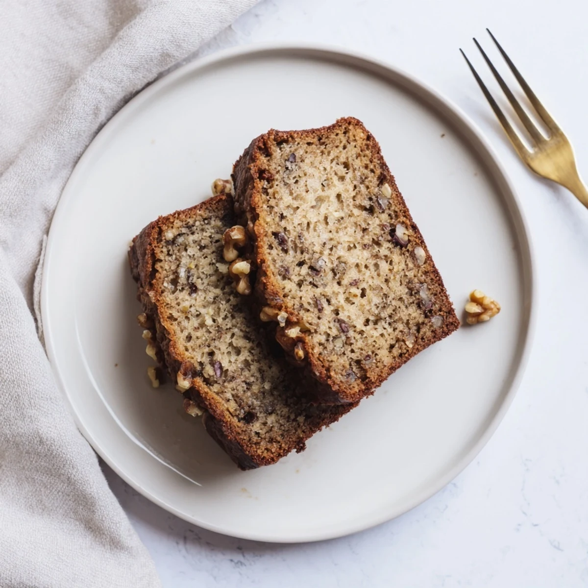 Slice of moist banana bread showing tender crumb, served on a white plate with walnuts