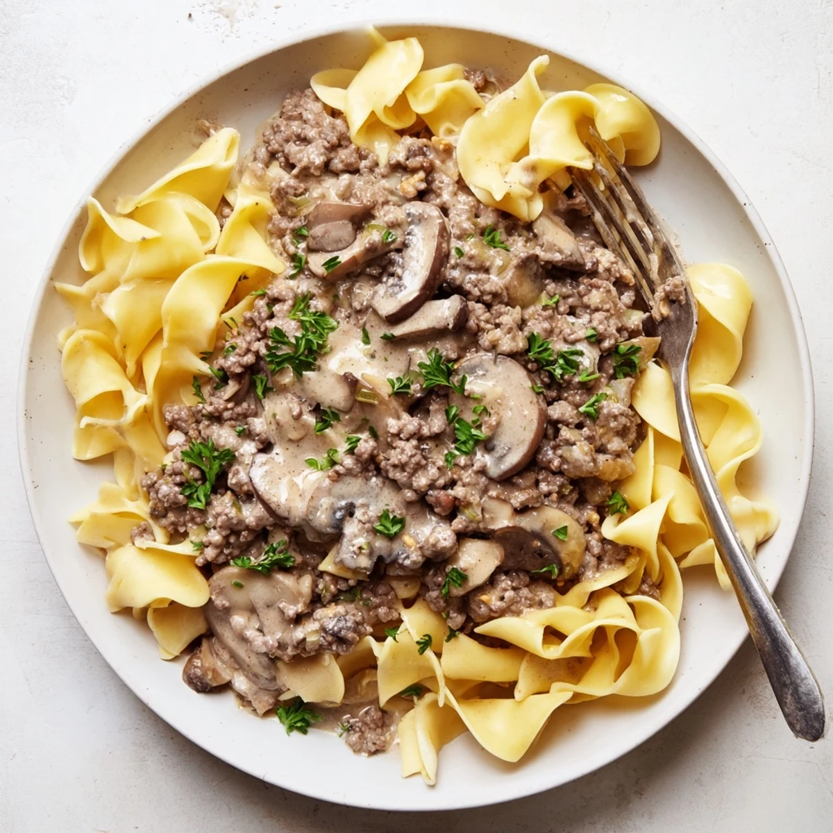 Creamy hamburger stroganoff with tender egg noodles, mushrooms, and fresh parsley garnish