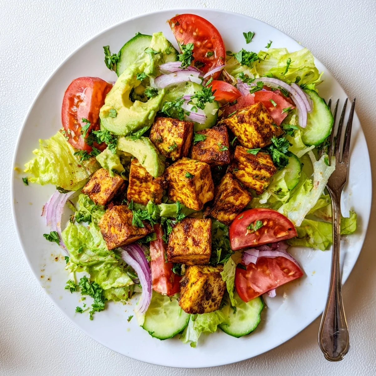 Vegan smoky tofu lettuce tomato salad plated with colorful vegetables and lemon herb dressing