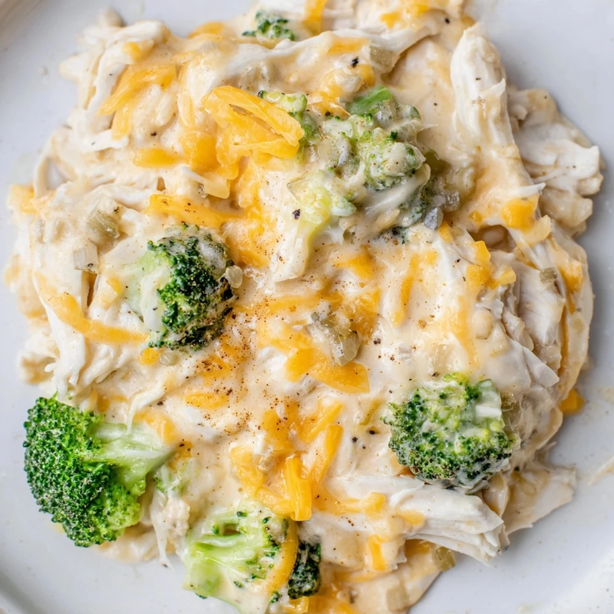 Slow cooker bowl featuring tender shredded chicken breast swimming in rich cheddar broccoli sauce