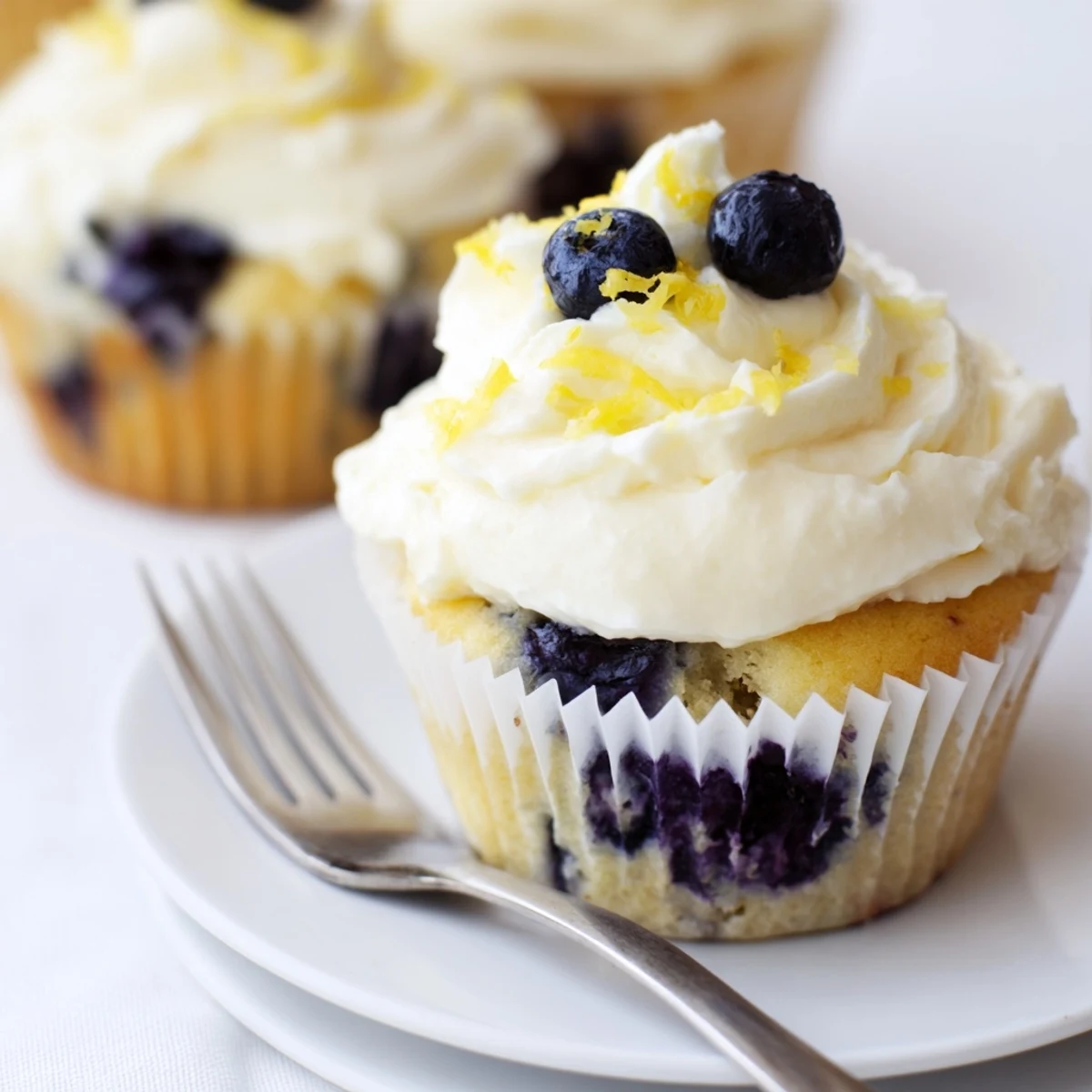 Golden lemon blueberry cupcakes topped with swirls of tangy cream cheese frosting and fresh berries