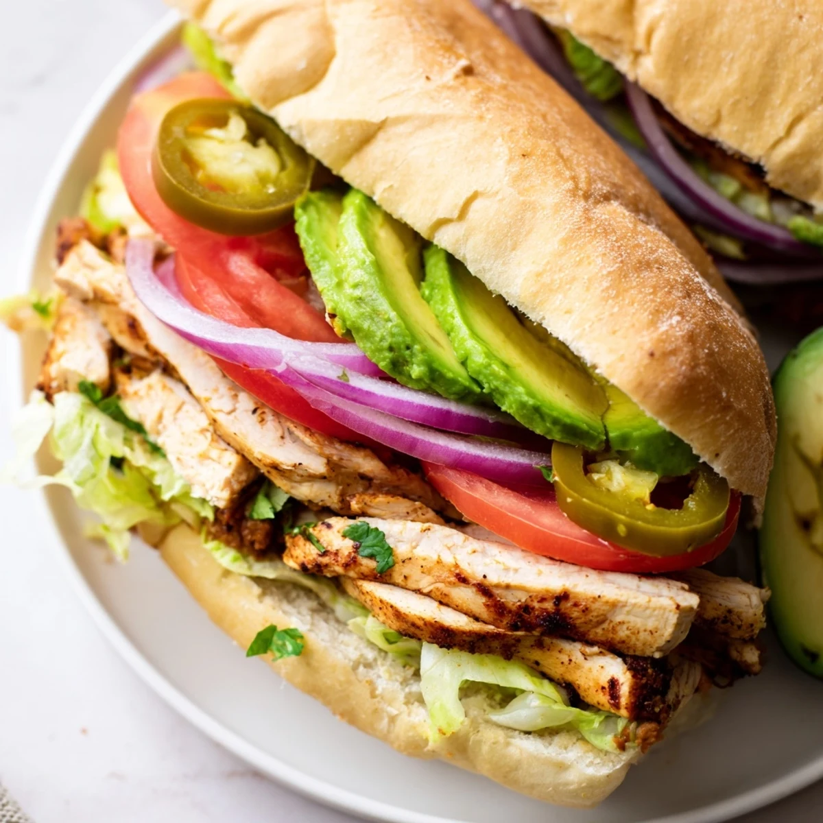Hearty chicken torta sandwich featuring marinated chicken breast with ripe tomato and red onion on soft roll