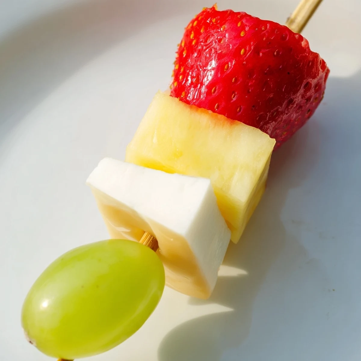 Colorful fruit and cheese kabobs arranged on a platter with red grapes strawberries pineapple and cheddar cubes