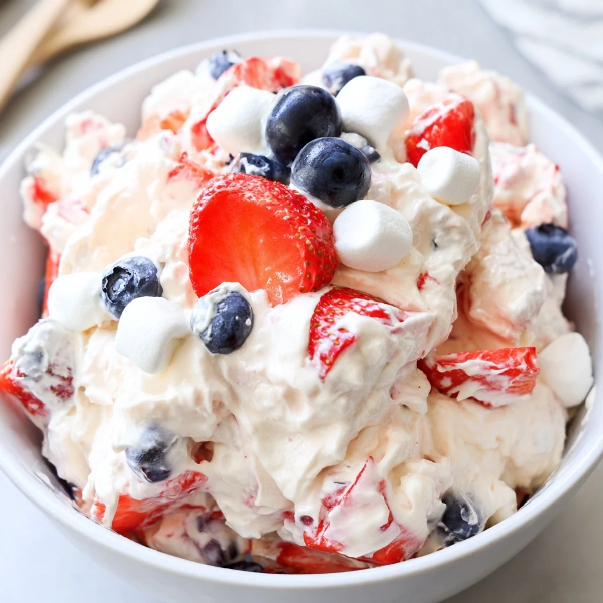 Red white blue cheesecake salad in a glass bowl garnished with strawberries