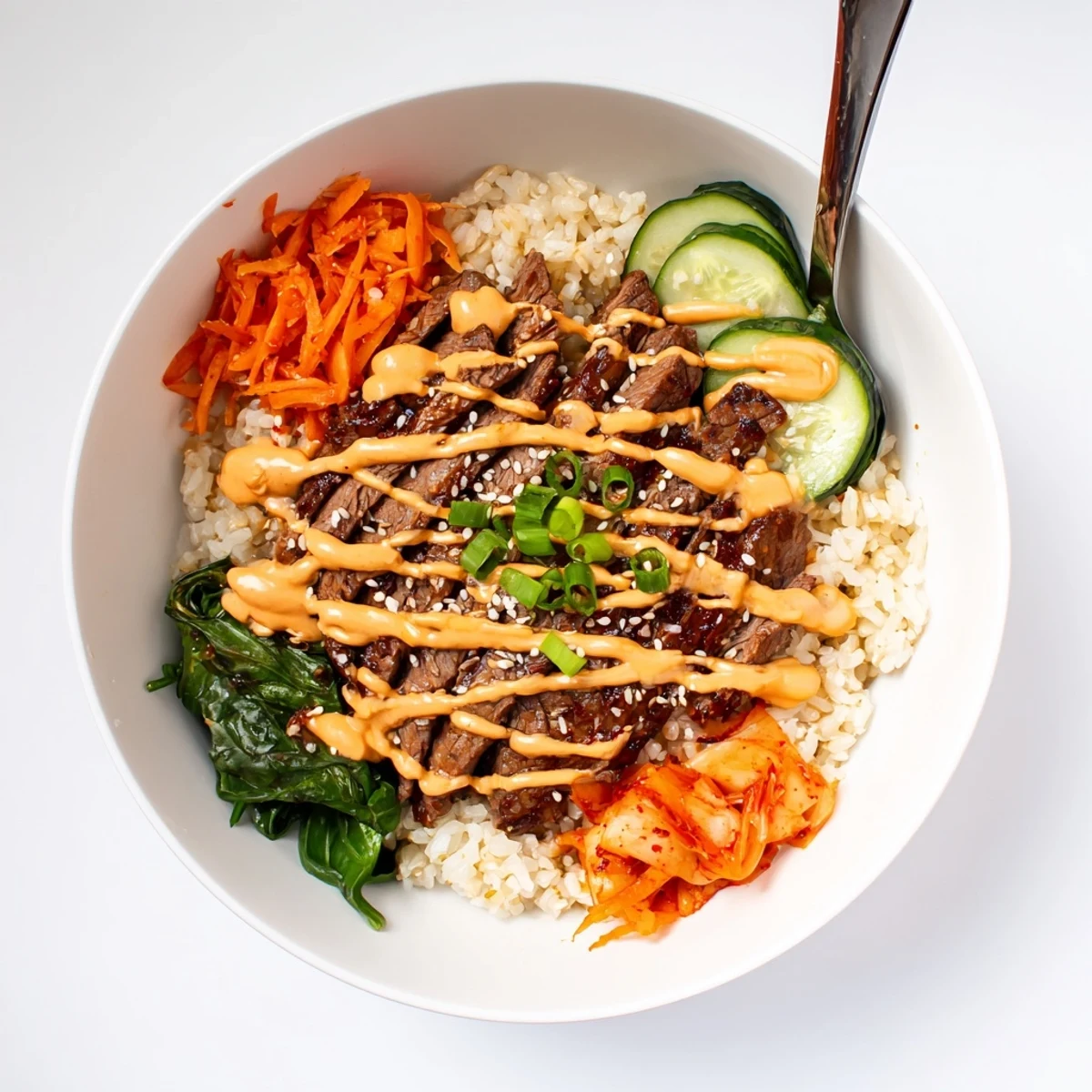 Caramelized marinated steak over fluffy jasmine rice in Korean BBQ Steak Rice Bowls with spicy cream sauce drizzled on top.