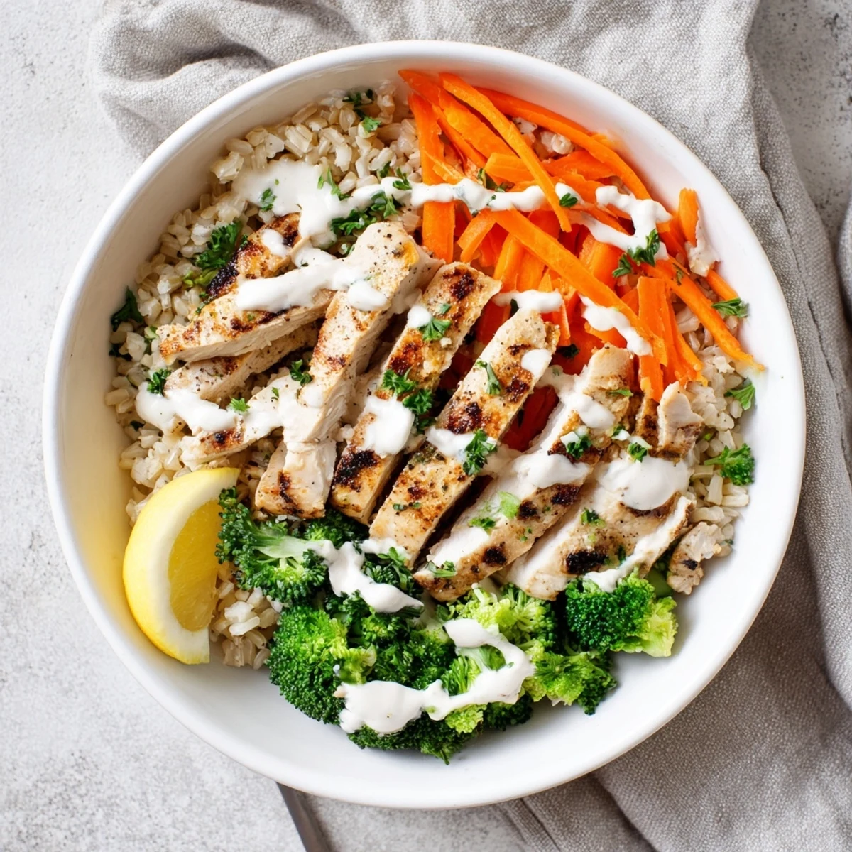 Vibrant grain bowl featuring tender grilled chicken strips, bright green broccoli, julienned carrots, and a tangy yogurt garlic sauce topping.