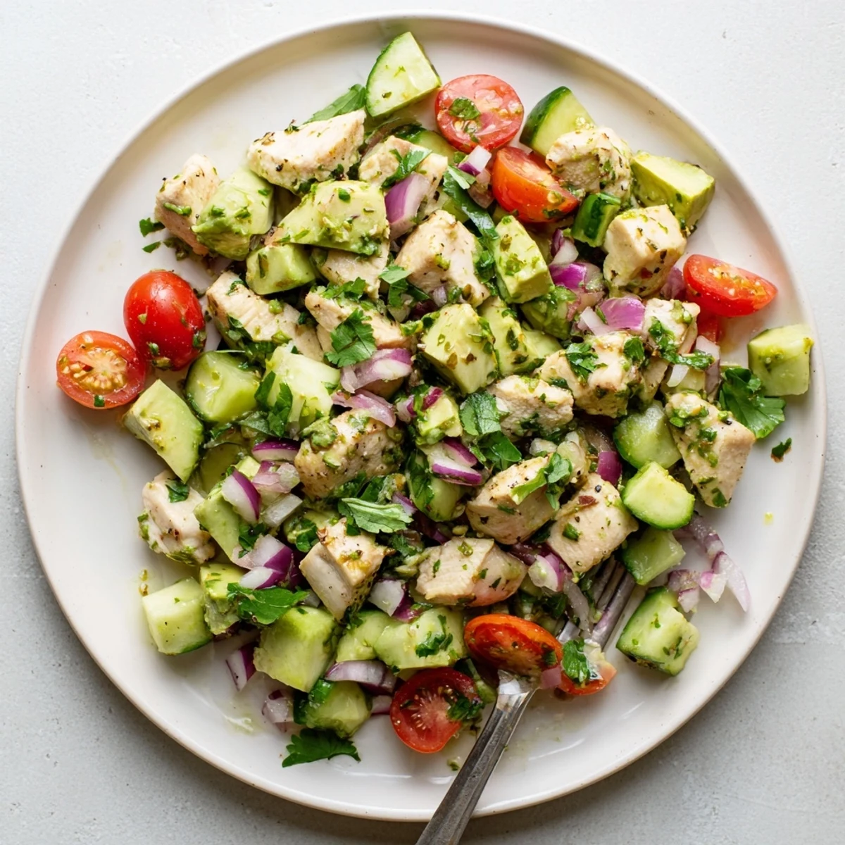 Colorful healthy avocado chicken salad bowl with grilled chunks, ripe avocado slices, and fresh vegetables drizzled with zesty lime dressing.