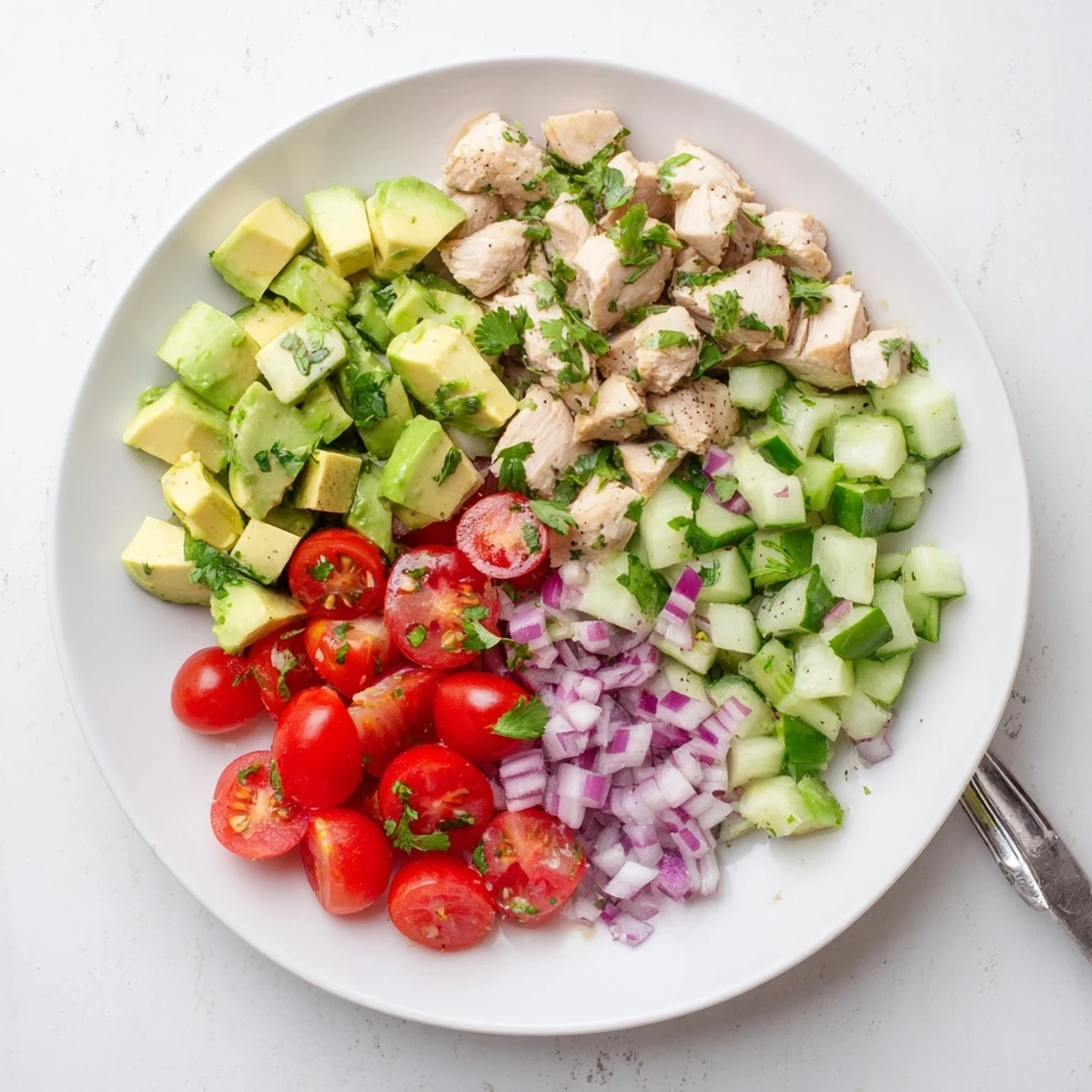 Fresh healthy avocado chicken salad plate featuring juicy diced chicken breast, creamy avocado, cherry tomatoes, and crisp cucumber tossed in tangy lime olive oil dressing.