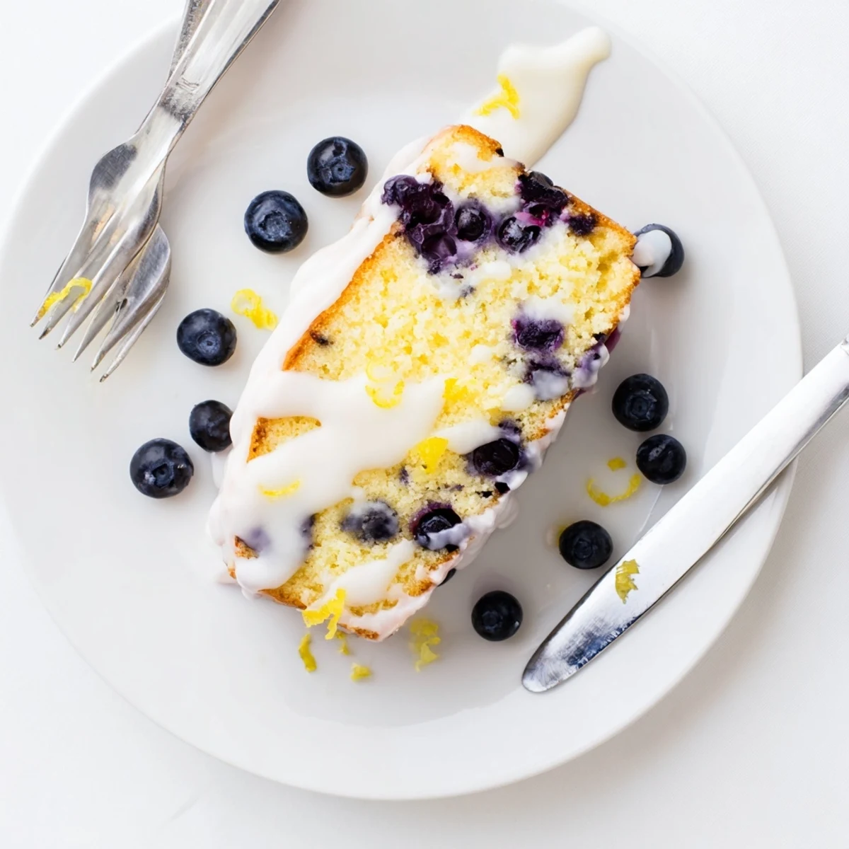 Moist lemon blueberry cake topped with sweet glaze and fresh juicy berries on a white serving plate