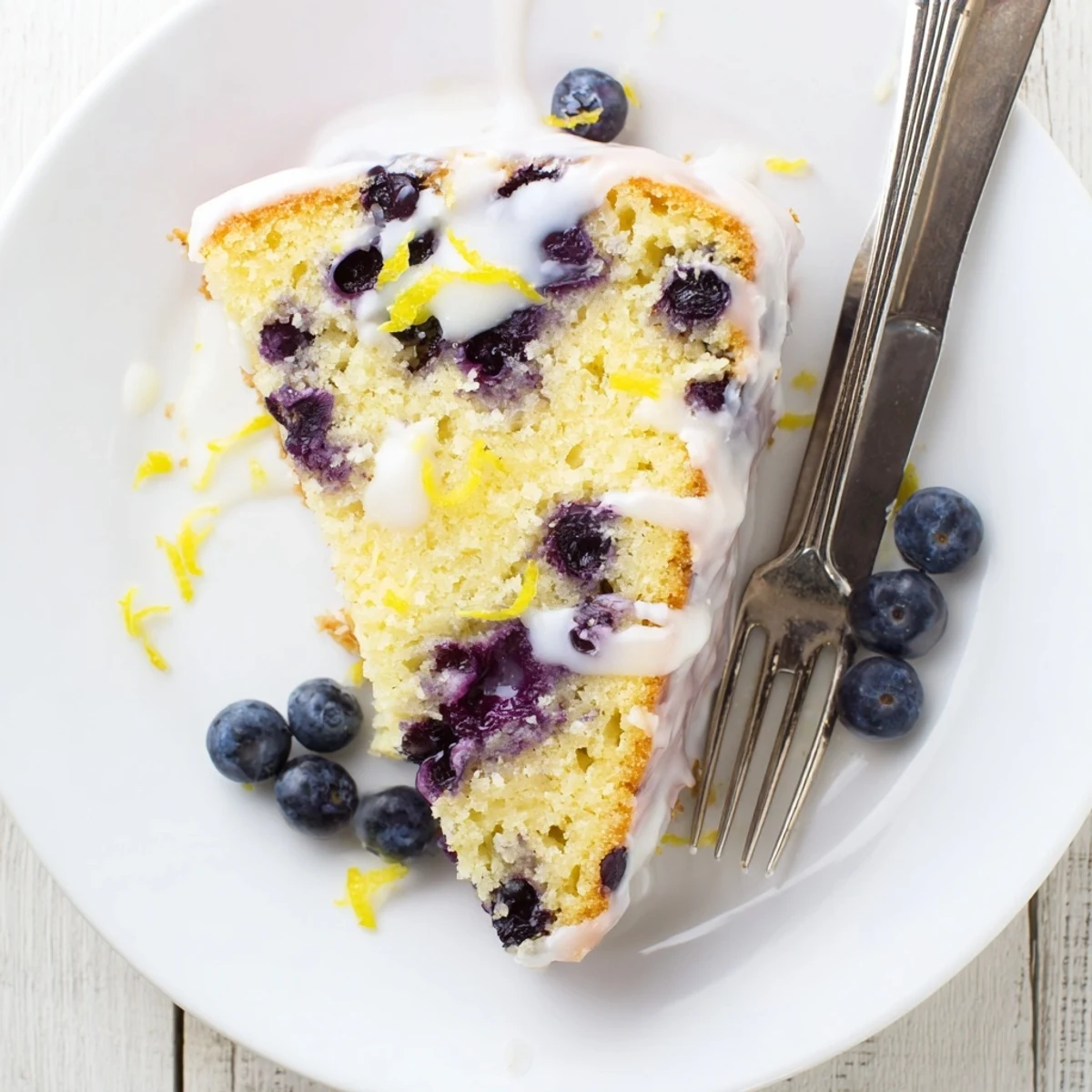 Golden lemon blueberry cake slice revealing tender blueberry-studded crumb with tangy lemon glaze dripping down the sides