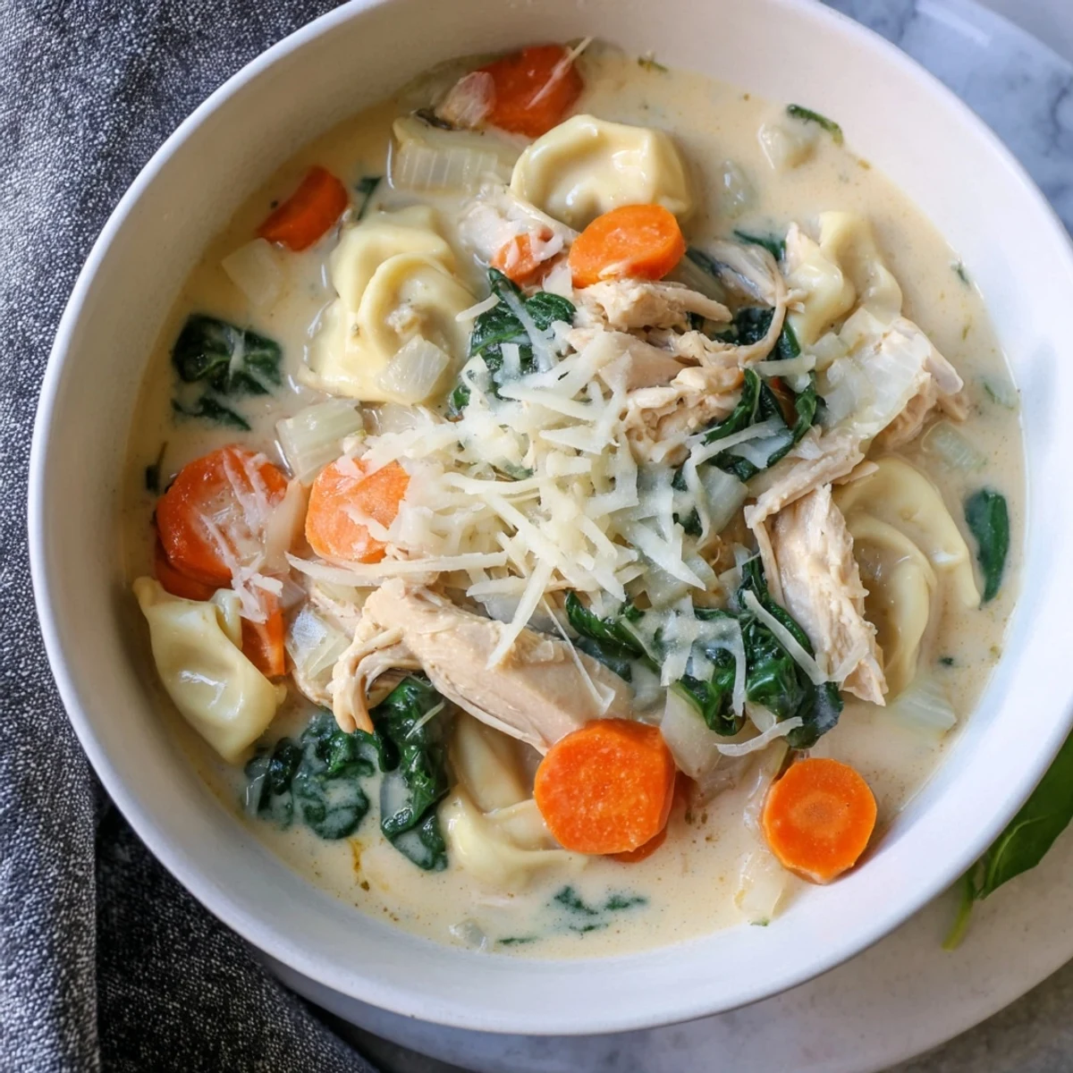 Creamy Crockpot Chicken Tortellini soup topped with parmesan and fresh baby spinach