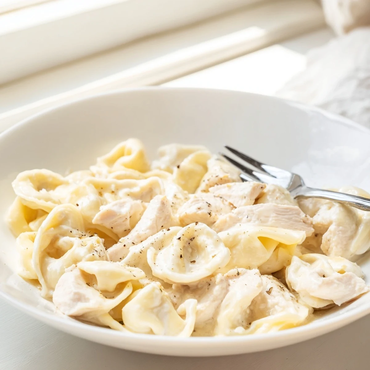 Golden chicken tortellini floating in a rich Parmesan cream sauce, garnished with parsley.