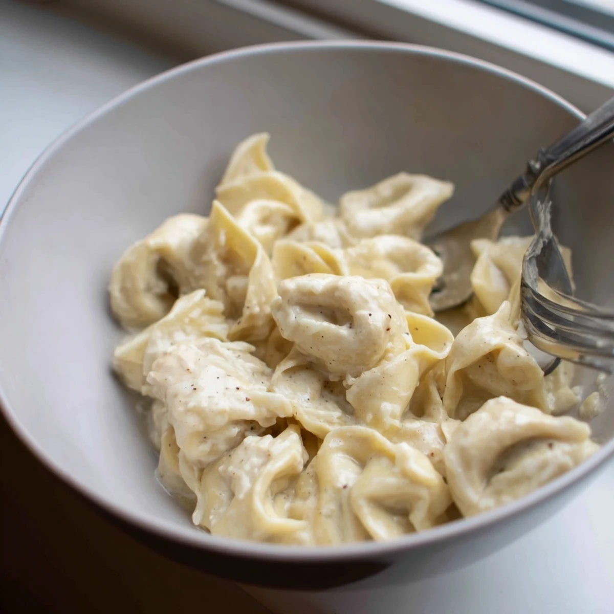 Close-up of homemade chicken tortellini pasta coated in a light white cream sauce.