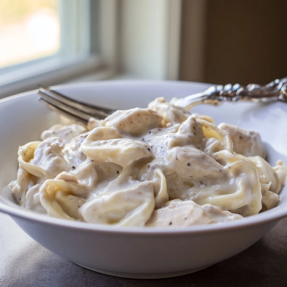 Bowl of savory chicken tortellini with fresh parsley and extra Parmesan cheese topping.