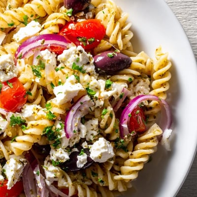 Tossed Mediterranean Pasta Salad featuring Kalamata olives, crisp cucumbers, and crumbled feta on a rustic wooden table.