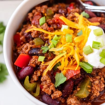 Hearty Slow Cooker Chili with Ground Beef ladled into a rustic bowl, topped with cheddar, sour cream, and chopped green onions.