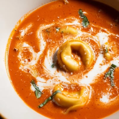 A pot of Creamy Tomato Tortellini Soup simmers with rich red broth, cheese tortellini, and herbs. 