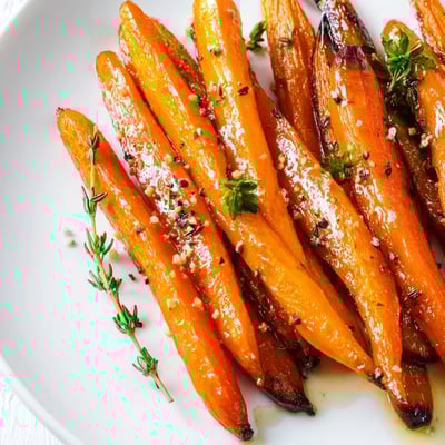 Freshly roasted carrots with honey and thyme garnished with parsley on a white plate. 