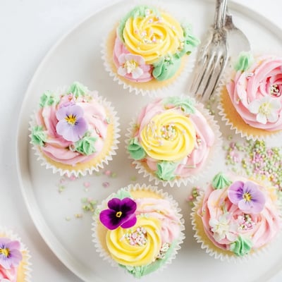 A close-up of Baby In Bloom Cupcakes decorated with pink and yellow buttercream flowers and edible pansies.
