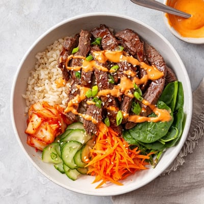 Crisp julienned veggies and chopped kimchi surround savory sliced beef in Korean BBQ Steak Rice Bowls finished with creamy Sriracha drizzle.